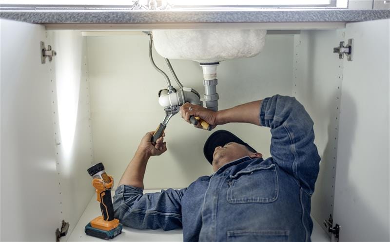 Plumber repairing pipes beneath a bathroom sink in Pomona